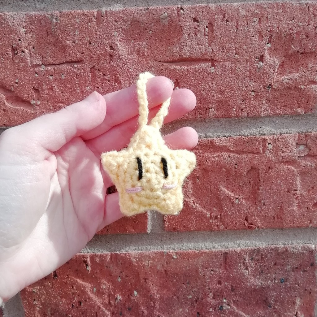 A yellow crochet plush star with a happy facial expression.